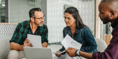 Two men and a woman casually dressed discussing a report in a professional setting